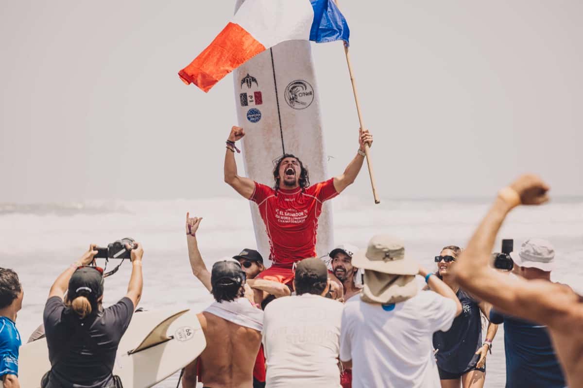 Foto de archivo: Edouard Delpero, con la lycra roja del Mundial, festeja en andas con los brazos en alto delante de su tabla y una bandera de Francia, tras ganar el oro en El Sunzal en 2025