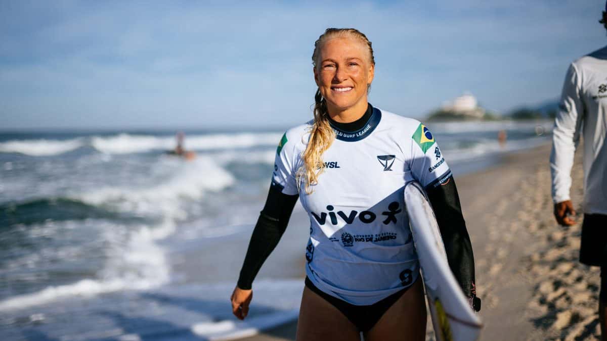 Tatiana Weston-Webb sonríe con la lycra del Vivo Rio Pro y la bandera de Brasil, con la tabla bajo el brazo en la playa de Saquarema, en junio de 2026 (foto de archivo)