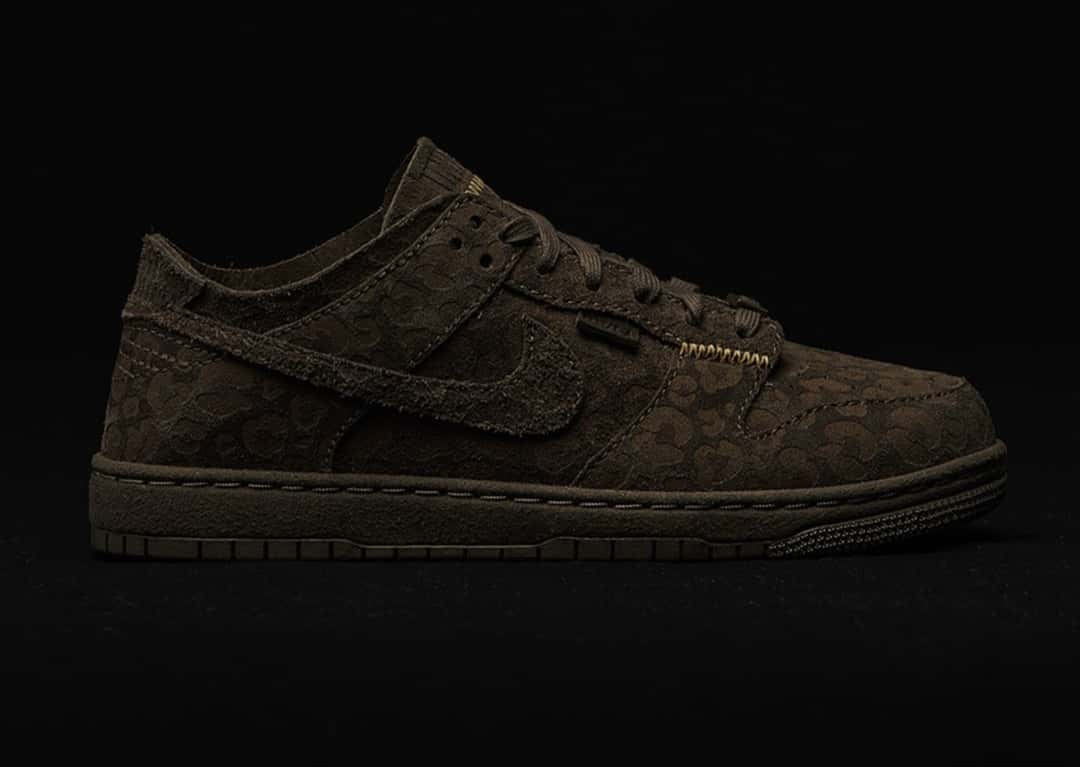 Union x Nike Dunk Low Natural Selection en marrón con estampa felina tonal, de perfil sobre fondo negro