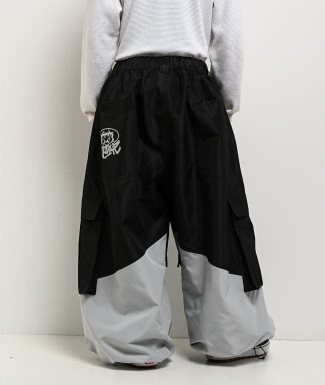 Vista trasera del pantalón de snowboard Empyre Tamarak ultra holgado, negro arriba y gris claro abajo, con bolsillos cargo laterales y un gráfico blanco en el bolsillo trasero